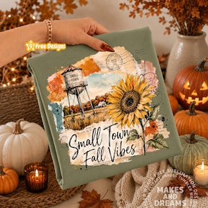 May include: An olive green fabric featuring a printed design of a water tower labeled Small Town, a large yellow sunflower, and the text Small Town Fall Vibes. The graphic includes watercolor-style splashes and a vintage postmark stamp.