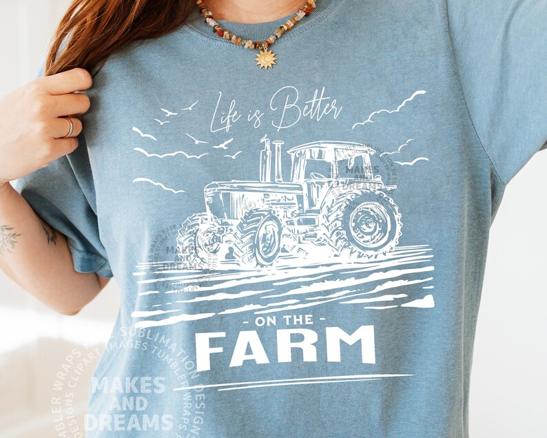 May include: A light blue t-shirt with a white graphic of a tractor and the text "Life is Better on the Farm." The design includes birds and clouds. The shirt is from the "Makes and Dreams" collection.