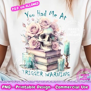 May include: A white t-shirt with a watercolor design featuring a skull, flowers, and candles. The text "You Had Me At" is written above the design. The text "Makes and Dreams" appears in a circle on the shirt. The text "Trigger Warning" is written below the design.