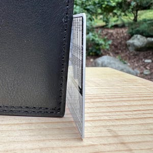 Plastic card leaning against a wallet to show the thickness of the card's plastic.