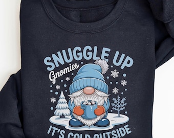 May include: Black sweatshirt with a winter gnome graphic. The gnome wears a blue hat and holds a mug. Text reads "Snuggle Up Gnomies, It's Cold Outside". Snowflakes and trees surround the gnome.