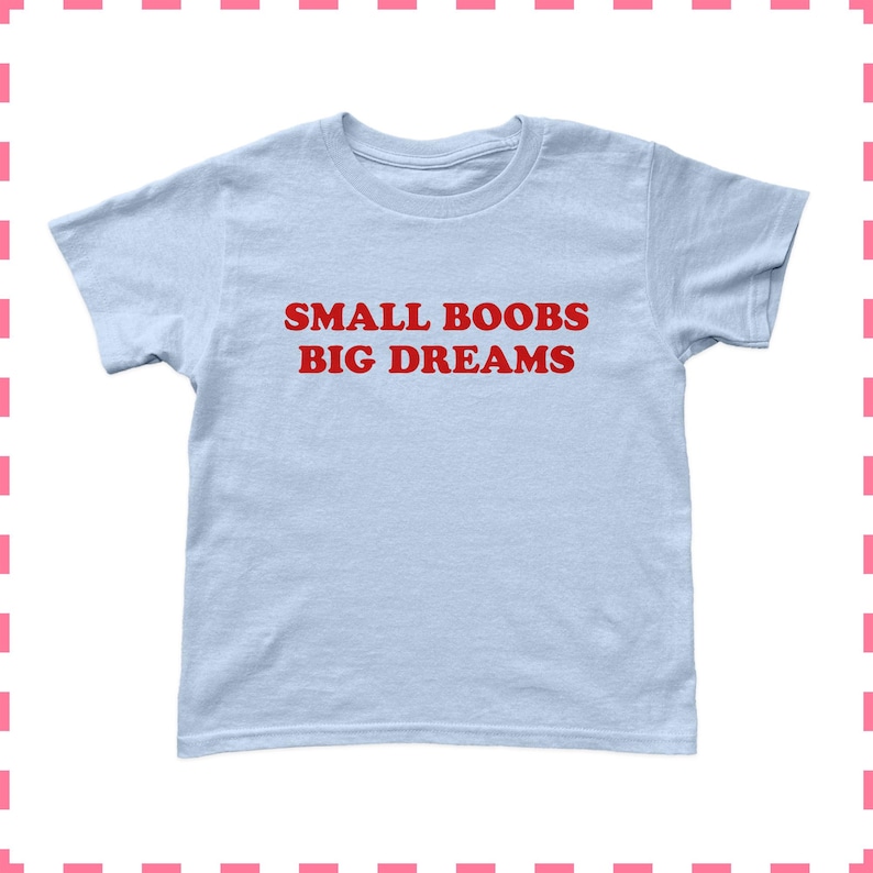 May include: A light blue t-shirt with the text "SMALL BOOBS BIG DREAMS" in red block letters. The shirt has short sleeves and a crew neck. The fabric appears to be a soft, lightweight material, suitable for casual wear.