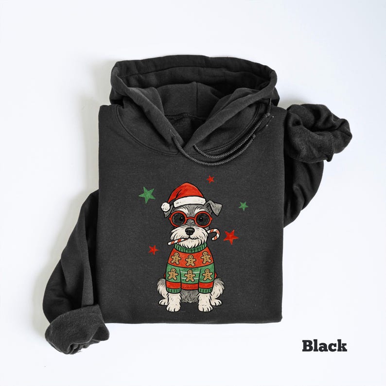 May include: Black hoodie featuring a cartoon dog wearing a Santa hat, glasses, and a gingerbread sweater. The dog is holding a candy cane. Green and red stars are scattered around the dog. The word "Black" is printed at the bottom.