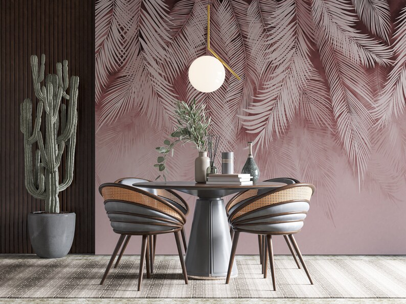 Pu&ograve; includere: Una sala da pranzo con una carta da parati a foglie tropicali rosa chiaro, un tavolo rotondo in legno con quattro sedie, una pianta di cactus in un vaso grigio e un lampadario a sospensione con un globo bianco.