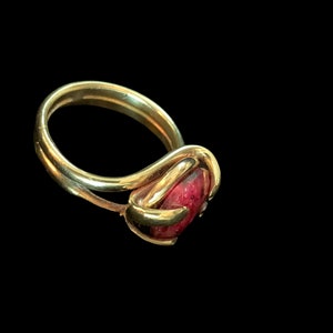 Puede incluir: Un anillo de oro con una piedra preciosa roja engastada en una banda retorcida.
