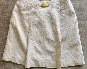 Puede incluir: Una falda de lino beige con un patrón de rayas blancas. La falda tiene un botón amarillo en la cintura.
