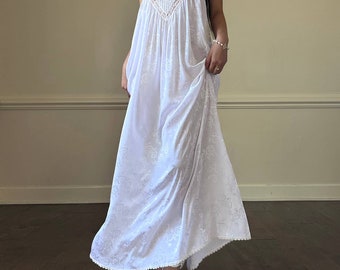 May include: A white maxi dress with a lace bodice and floral embroidery. The dress has thin straps and a scalloped hem.
