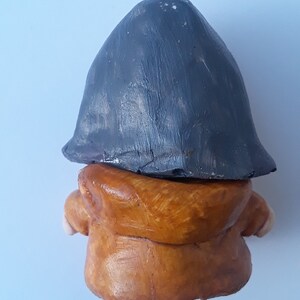 May include: A small clay figurine of a person wearing a brown hooded jacket and a gray hat.
