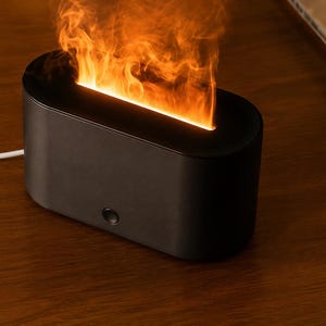 May include: A black, rectangular electric fireplace with a flame effect. The device has a rounded top and a single button on the front. A white power cord extends from the back. The flame effect emits orange and yellow light.
