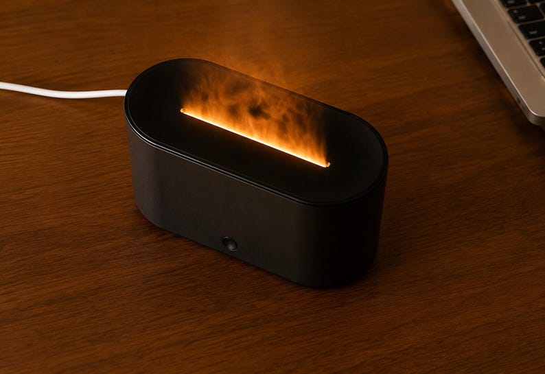 May include: A black, oval aromatherapy diffuser with an orange flame effect. The diffuser is on a wooden surface. A white power cord extends to the left. The device is approximately 20 cm long.