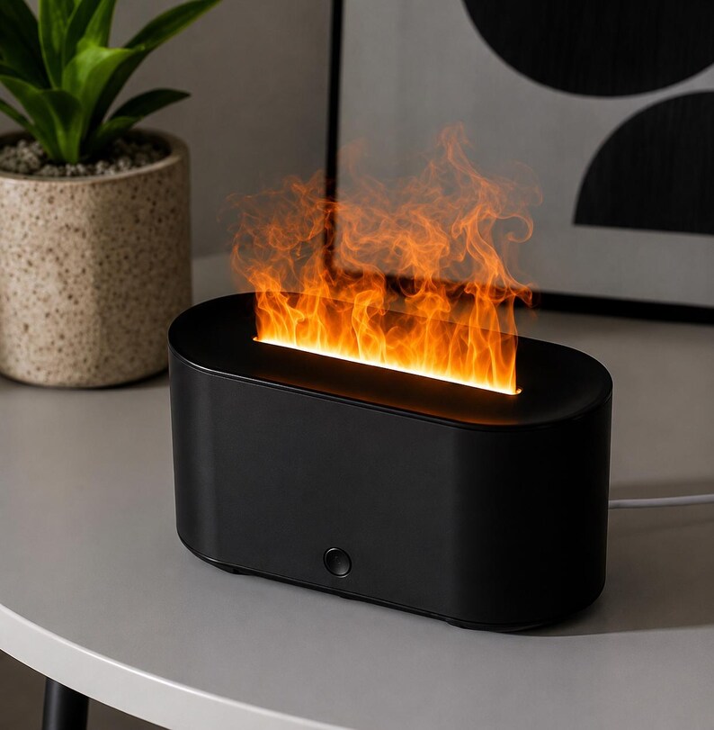 May include: A black, oval electric fireplace with a simulated flame effect. The unit sits on a grey surface, with a small button on the front. The flames are orange and yellow, creating a warm atmosphere. A decorative plant is in the background.