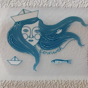 Op de afbeelding: Een blauwe en witte illustratie van een vrouw met lang haar die een matrozenhoed draagt. Het haar van de vrouw is golvend gestyled en er zijn twee kleine papieren bootjes en een vis in de afbeelding. De tekst "fernweh" staat in de afbeelding.