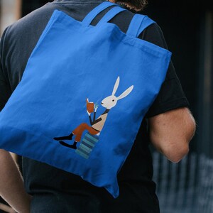 May include: A blue tote bag with a white rabbit illustration holding a cup and a book while sitting on a stack of books.