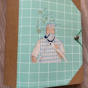 Może przedstawiać: Zielony i brązowy segregator z tkaniny w kratkę. Na przedniej okładce znajduje się rysunek mężczyzny z brodą i fajką, który nosi sweter i trzyma fajkę. Mężczyzna jest otoczony zielonymi winoroślami.