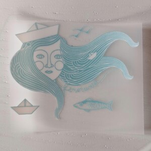 May include: A light blue and white illustration of a woman with flowing hair, wearing a paper hat, and a fish. The illustration also includes a paper boat, seagulls, and the word "kernweh".