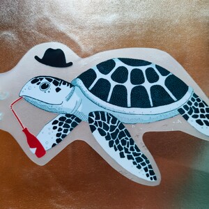 Op de afbeelding: Een cartoonillustratie van een zeeschildpad die een zwarte fedora draagt en drinkt uit een rood-wit gestreepte rietje. De schildpad houdt een rode fles in zijn rechtervin en een garnaal met rode kersen bevindt zich aan de linkerkant van de afbeelding.