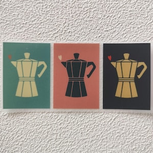 Può includere: Tre illustrazioni di una caffettiera con un cuore sopra ciascuna. Le caffettiere sono di colori diversi: turchese, rosa e nero. Le caffettiere sono bianche, nere e dorate.