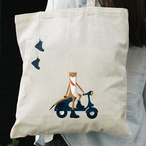 Può includere: Una borsa tote bianca con un'illustrazione di un furetto che guida uno scooter blu. Il furetto indossa una sciarpa rossa e ha una coda marrone. Due stivali blu pendono dalla parte superiore della borsa.