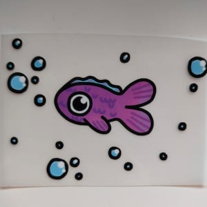 Könnte beinhalten: Ein lila Fisch mit einem großen Auge und einer blauen Flosse schwimmt durch ein Feld aus weißen Blasen.