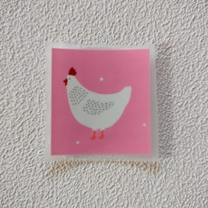 Può includere: Un pollo bianco con cresta e bargigli rossi è illustrato su uno sfondo rosa con pois bianchi.