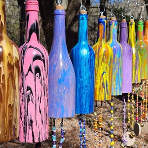 May include: A colorful wind chime made from recycled wine bottles. Each bottle is hand-painted with a unique marbled design in various colors, including brown, pink, blue, yellow, purple, green, and orange. The bottles are strung together with beads and charms, creating a whimsical and decorative piece.