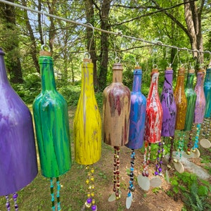 May include: A collection of colorful glass bottles with beads hanging from them. The bottles are painted in various shades of purple, green, yellow, brown, blue, and red. The bottles are hung from a wire and are arranged in a row.