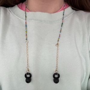 May include: A beaded eyeglass chain with colorful beads and gold-colored chain accents. The chain has black earbud holders at the ends. The chain is worn around the neck.