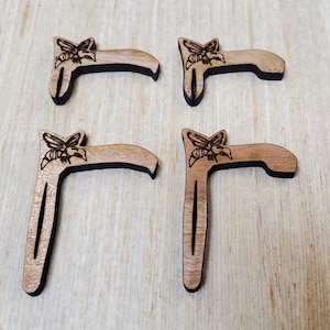 May include: Four wooden bookmarks with a bee design. Each bookmark is shaped like a letter T with a bee design at the top.