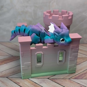 May include: A 3D-printed toy castle with a pink and green gradient, featuring a matching pink tower. A colorful dragon with blue and purple hues rests on the castle walls. The dragon has white wings and a friendly expression.