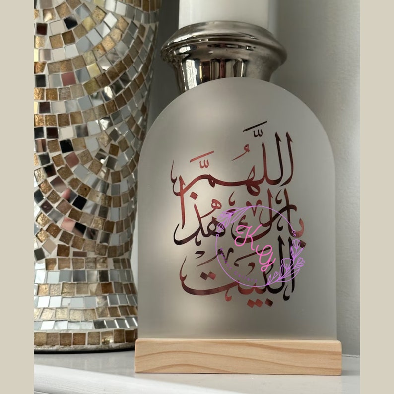 May include: A frosted glass arch with a wooden base, featuring Arabic calligraphy in a rose gold color. The calligraphy reads "Allahumma inni as'aluka al-jannah".