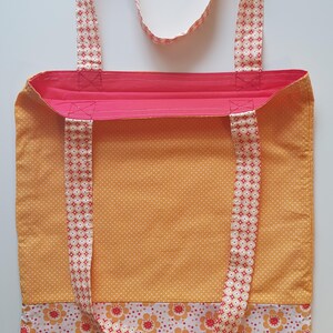 Könnte beinhalten: Handgefertigte Tragetasche mit lebendigem Design. Die Tasche hat ein gelbes Tupfenmuster auf dem Hauptteil, einen floral gemusterten Boden und einen rosa Innenraum. Die Träger sind mit roten und weißen geometrischen Formen gemustert. Der Text "Variante 5" ist sichtbar.