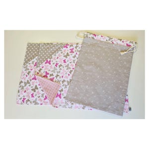 Könnte beinhalten: Ein Set aus vier Stoffquadraten mit einem Schmetterlingsmuster in Rosa und Weiß auf beigefarbenem Hintergrund. Die Quadrate sind gefaltet und übereinander gestapelt. Es gibt auch eine beigefarbene Kordeltasche mit einem Schmetterlingsmuster in Rosa und Weiß.