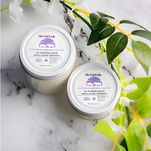 May include: Two white jars with gold lids containing lavender whipped tallow all-purpose cream. The jars have a purple and white label with the text "The Fat Lady" and "Lavender Whipped Tallow All Purpose Cream" on them.