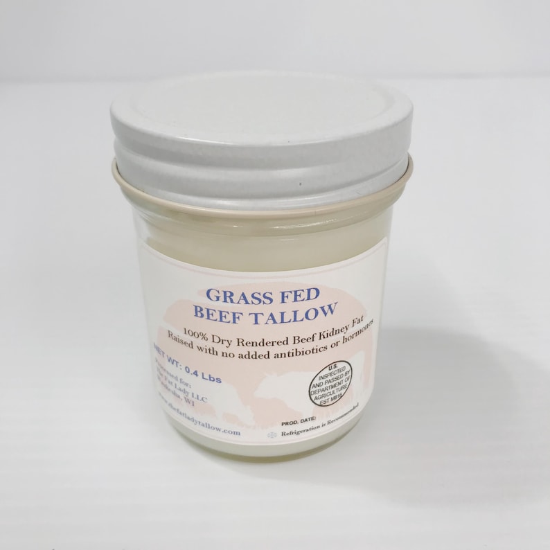May include: A clear glass jar with a white metal lid containing off-white beef tallow. The label reads Grass Fed Beef Tallow, 100% Dry Rendered Beef Kidney Fat, Raised with no added antibiotics or hormones, and Net Wt: 0.4 Lbs.