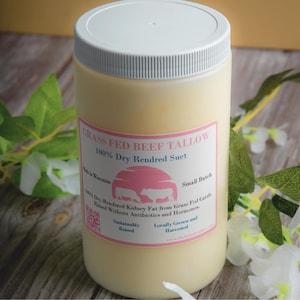 May include: A white jar with a yellow label that reads "GRASS FED BEEF TALLOW 100% Dry Rendred Suet". The label also includes the text "Small Batch", "100% Dry-Rendered Kidney Fat from Grass Fed Cattle Raised Without Antibiotics and Hormones", "Sustainably Raised", and "Locally Grown and Harvested".