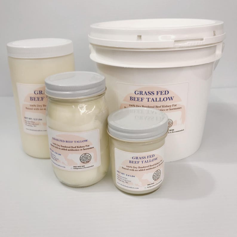 May include: A collection of four containers of grass fed beef tallow, including one large white plastic bucket and three glass jars of varying sizes, all featuring white lids and labels with the text Grass Fed Beef Tallow and net weights.