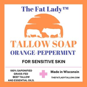 Puede incluir: Jab&oacute;n de sebo de naranja y menta para pieles sensibles. La etiqueta presenta una puesta de sol con dos vacas y el texto "The Fat Lady TM". Tambi&eacute;n indica que el jab&oacute;n est&aacute; hecho con 100% de sebo de res alimentado con pasto saponificado y aceites esenciales. La etiqueta tambi&eacute;n indica "Hecho en Wisconsin" e incluye el sitio web "thefatladytallow.com".