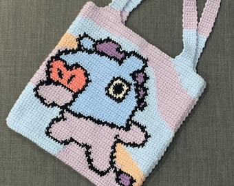 May include: A crocheted tote bag with a cartoon character design. The bag is made with a variety of colors, including pink, blue, and orange. The character is a blue creature with a pink heart and a yellow eye.