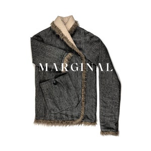 Puede incluir: Una chaqueta de tweed gris con cuello y ribetes de piel sintética marrón. La chaqueta tiene un cierre de botón único y un bolsillo de parche en el lado izquierdo. La palabra "MARGINAL" está impresa en la parte delantera de la chaqueta.