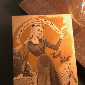 May include: A vintage advertisement for Berth Robert featuring a woman in a gray dress and a white blouse. The text reads "Back to School and Early Fall Fashions".