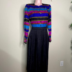 May include: A vintage two-piece dress featuring a striped button-up top in blue, purple, and black with gold accents, paired with a black, patterned midi skirt. The dress is displayed on a mannequin.