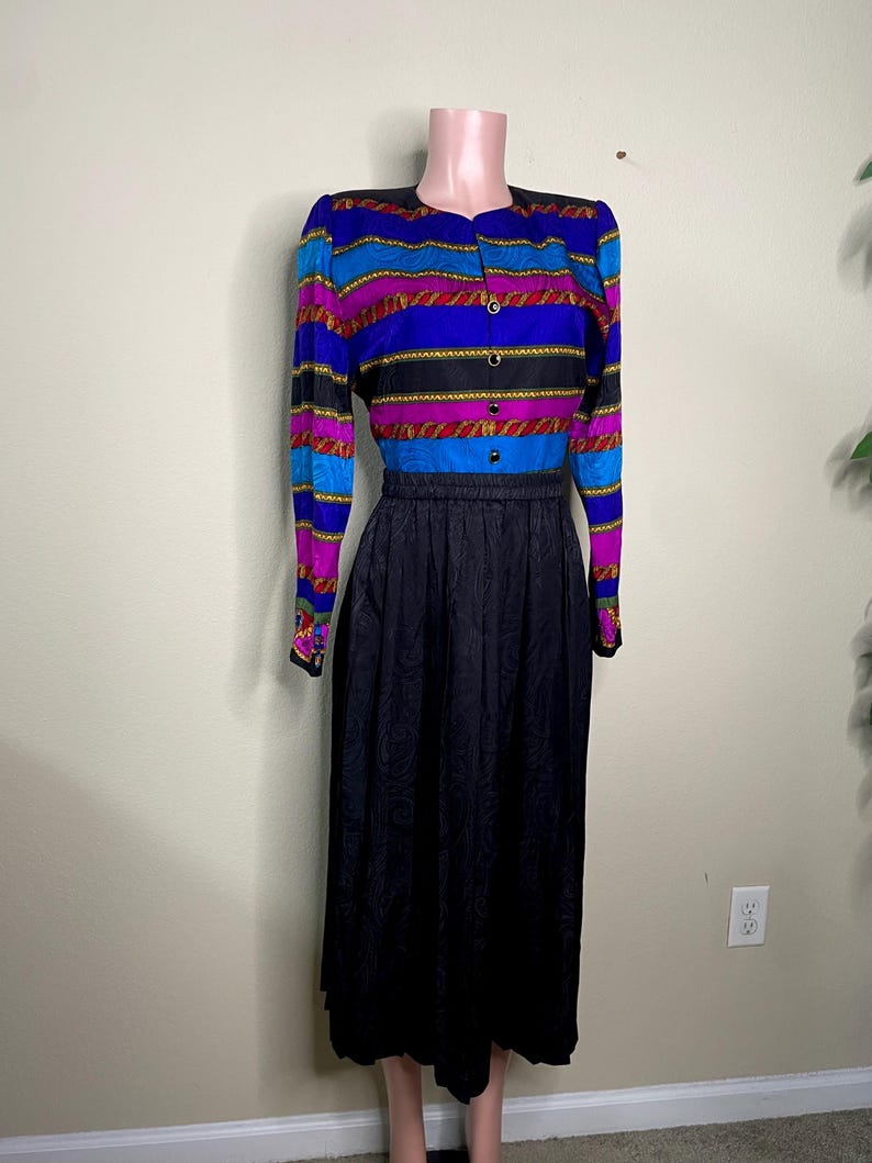 May include: A vintage two-piece dress featuring a striped button-up top in blue, purple, and black with gold accents, paired with a black, patterned midi skirt. The dress is displayed on a mannequin.