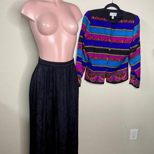 May include: A black paisley print skirt and a colorful button-up jacket with a black collar and gold trim are displayed on a mannequin. The jacket features horizontal stripes in blue, purple, and red.