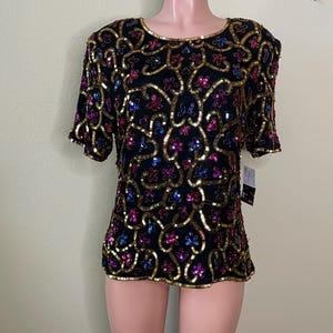 May include: A black sequined top with gold, pink, and blue sequins in a floral pattern. The top has short sleeves and a round neckline.
