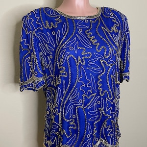 May include: A royal blue silk blouse with a gold and silver beaded design. The blouse has a round neckline and short sleeves.