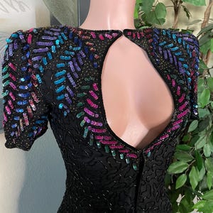 May include: Black sequined dress with colorful sequin detailing on the shoulders and neckline. The dress has short sleeves and a keyhole back. The sequins are in shades of pink, purple, blue, and green.