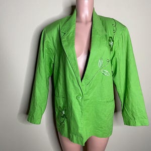 May include: Bright green blazer with long sleeves and a single-button closure. The blazer features embroidered floral designs in white and green. The garment is displayed on a mannequin.