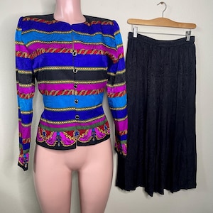 May include: A vintage two-piece suit featuring a colorful, patterned jacket and a black skirt. The jacket has a button-up front and a vibrant design with blue, purple, and red stripes. The skirt is a solid black color.