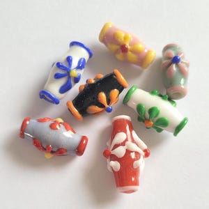 May include: A selection of vibrant glass beads with floral designs. The beads are in various shapes, including cylindrical and rounded, and feature patterns in red, orange, yellow, blue, green, and white. The beads are ideal for jewellery making.