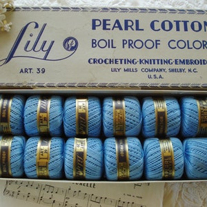 May include: A box of blue Lily Pearl Cotton thread, labeled "Art. 39" and "Boil Proof Colors". The box is open and the spools of thread are visible. The box is labeled "Crocheting Knitting Embroidery" and "Lily Mills Company, Shelby, N.C. U.S.A."